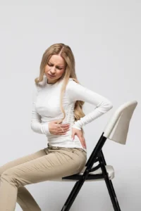 Woman holding her lower back in pain from a pinched nerve, a common condition that can cause sciatica and leg pain, treated at Frisco Spinal Rehab with spinal decompression and chiropractic care.